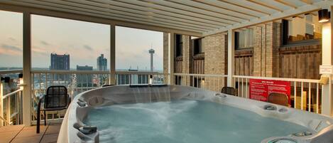 A hot tub with a control panel, a chair, and a view of the cityscape.