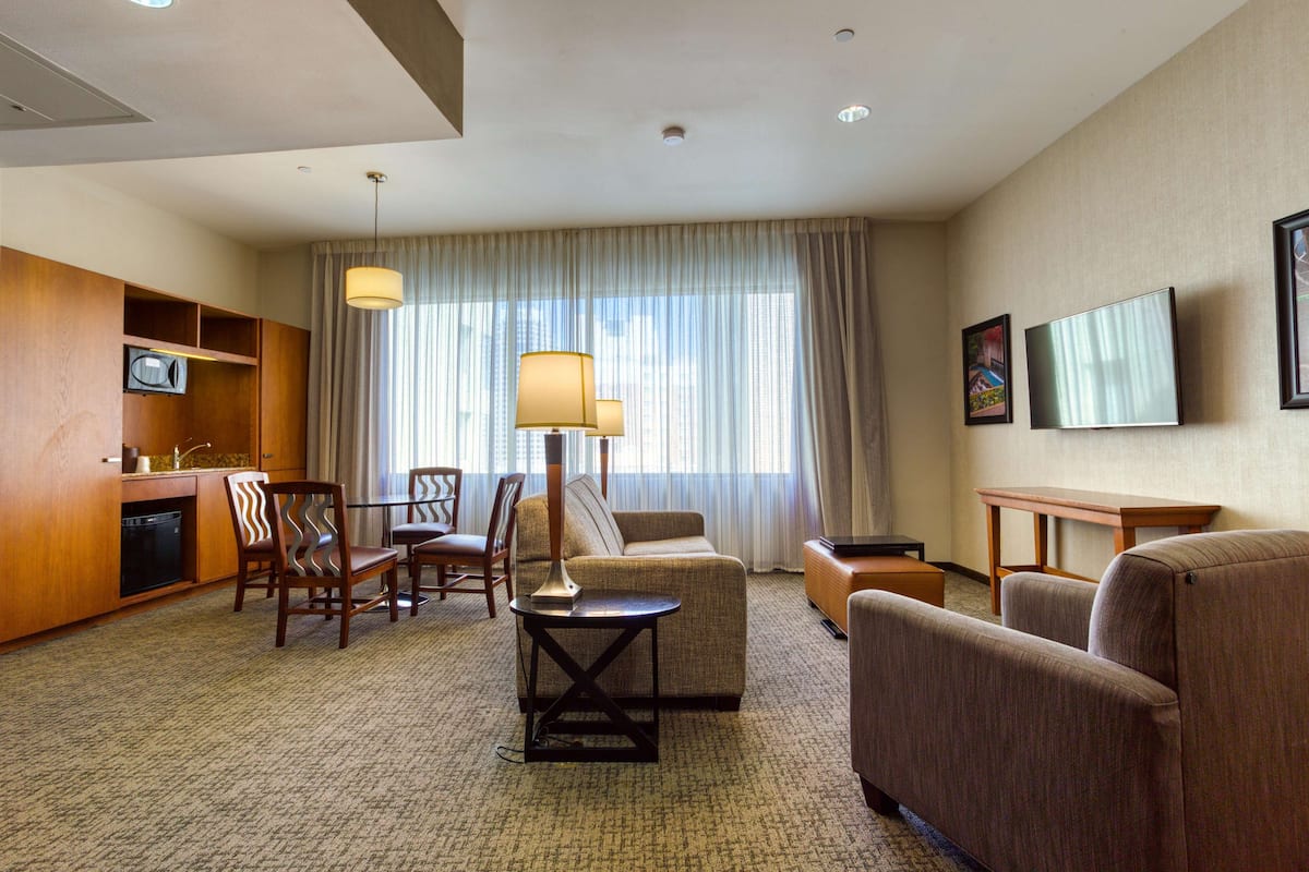 Une chambre d’hôtel équipée d’un canapé, de fauteuils, d’une petite table, d’une télévision, d’un bureau et d’un coin cuisine avec un four à micro-ondes.
