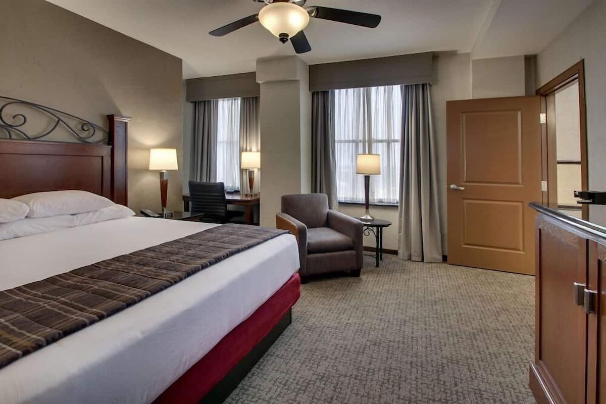 A hotel room with a bed, a desk, a chair, a door, and a ceiling fan.