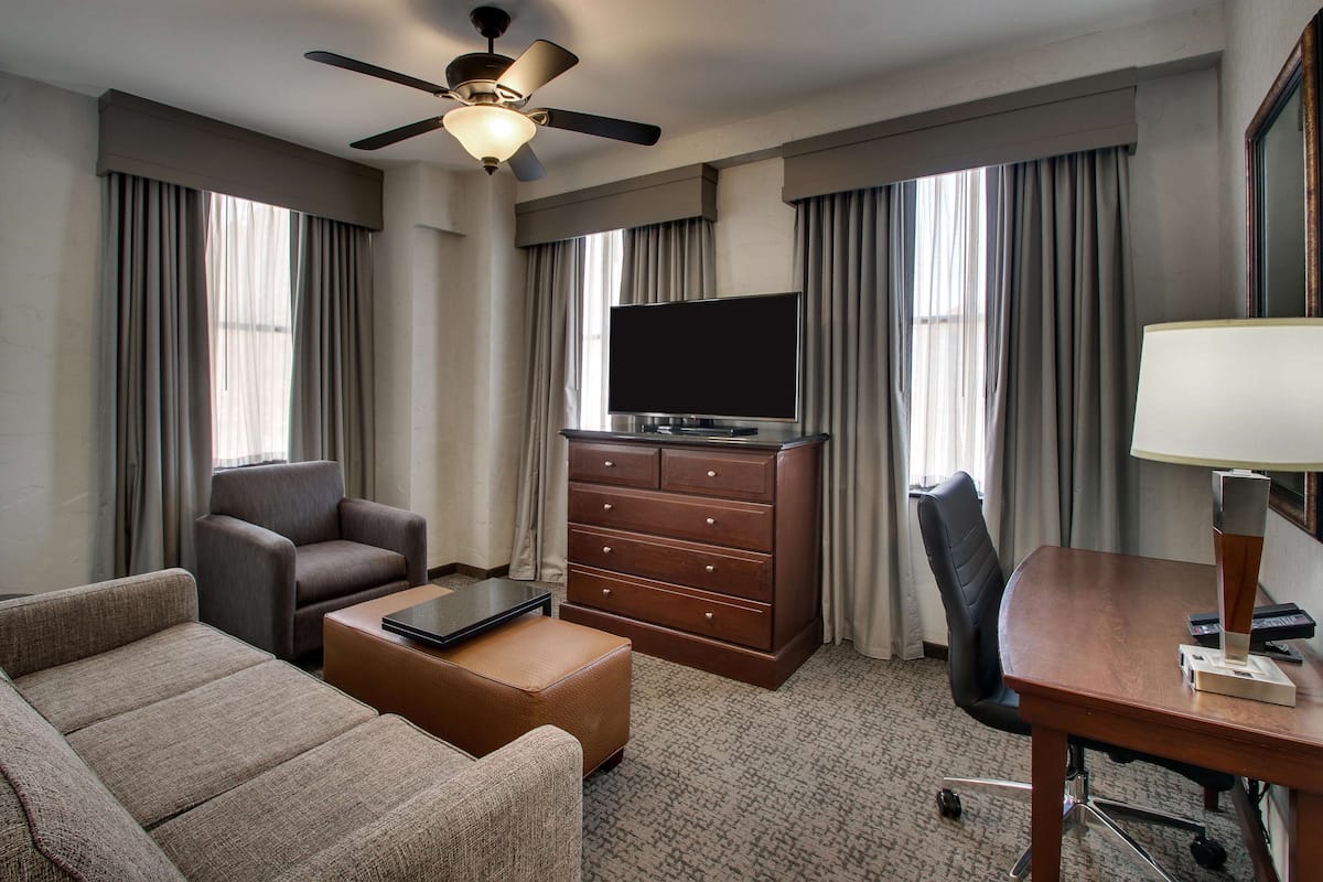 Une chambre d’hôtel équipée d’un canapé, d’un bureau, d’une commode, d’une télévision et d’un ventilateur de plafond.
