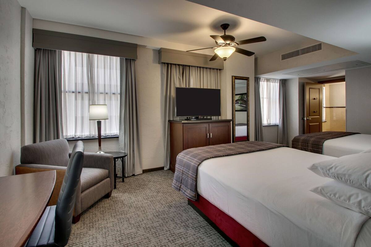 Une chambre d’hôtel équipée d’un lit, d’un bureau, d’une chaise, d’une télévision et d’un ventilateur de plafond.