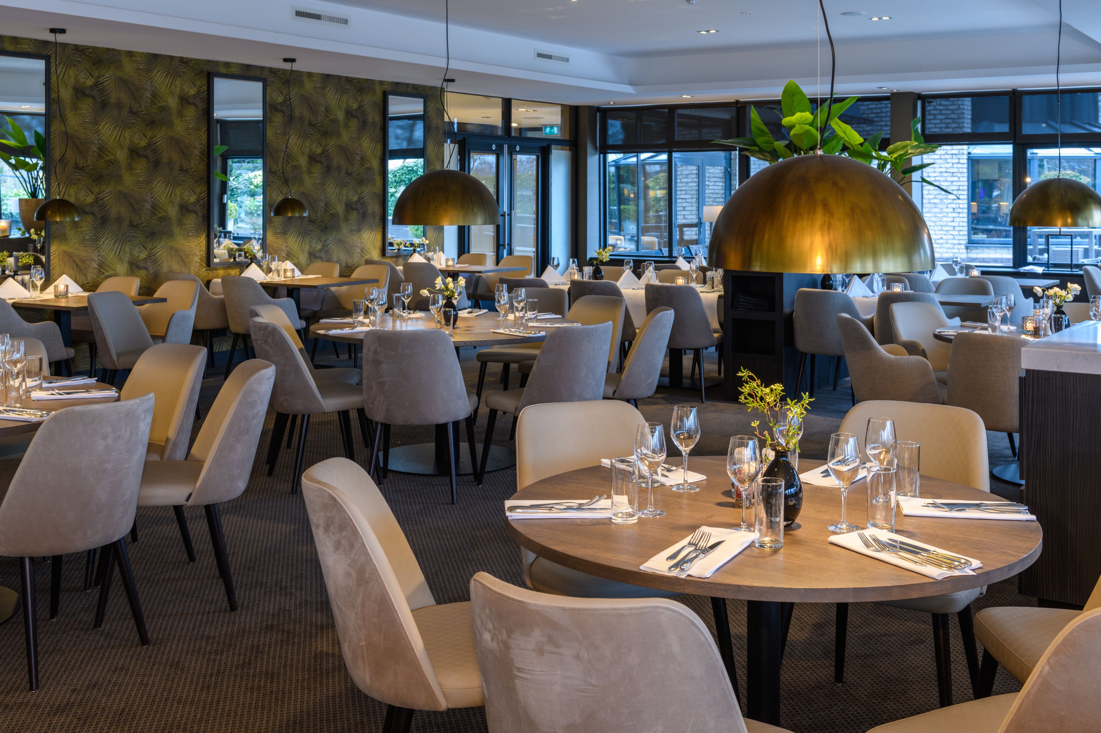 A modern restaurant with round tables, comfortable chairs, and large pendant lights.