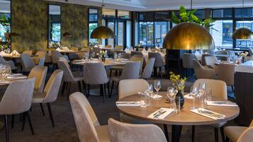 A modern restaurant with round tables, comfortable chairs, and large pendant lights.