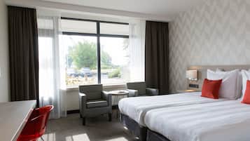 Een hotelkamer met een bed, twee stoelen, een tafeltje en een raam met gordijnen.