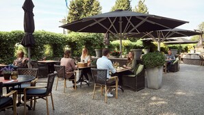 Un espace extérieur aménagé en terrasse, avec des tables rondes et des chaises en osier, entouré de plantes en pot et de parasols.