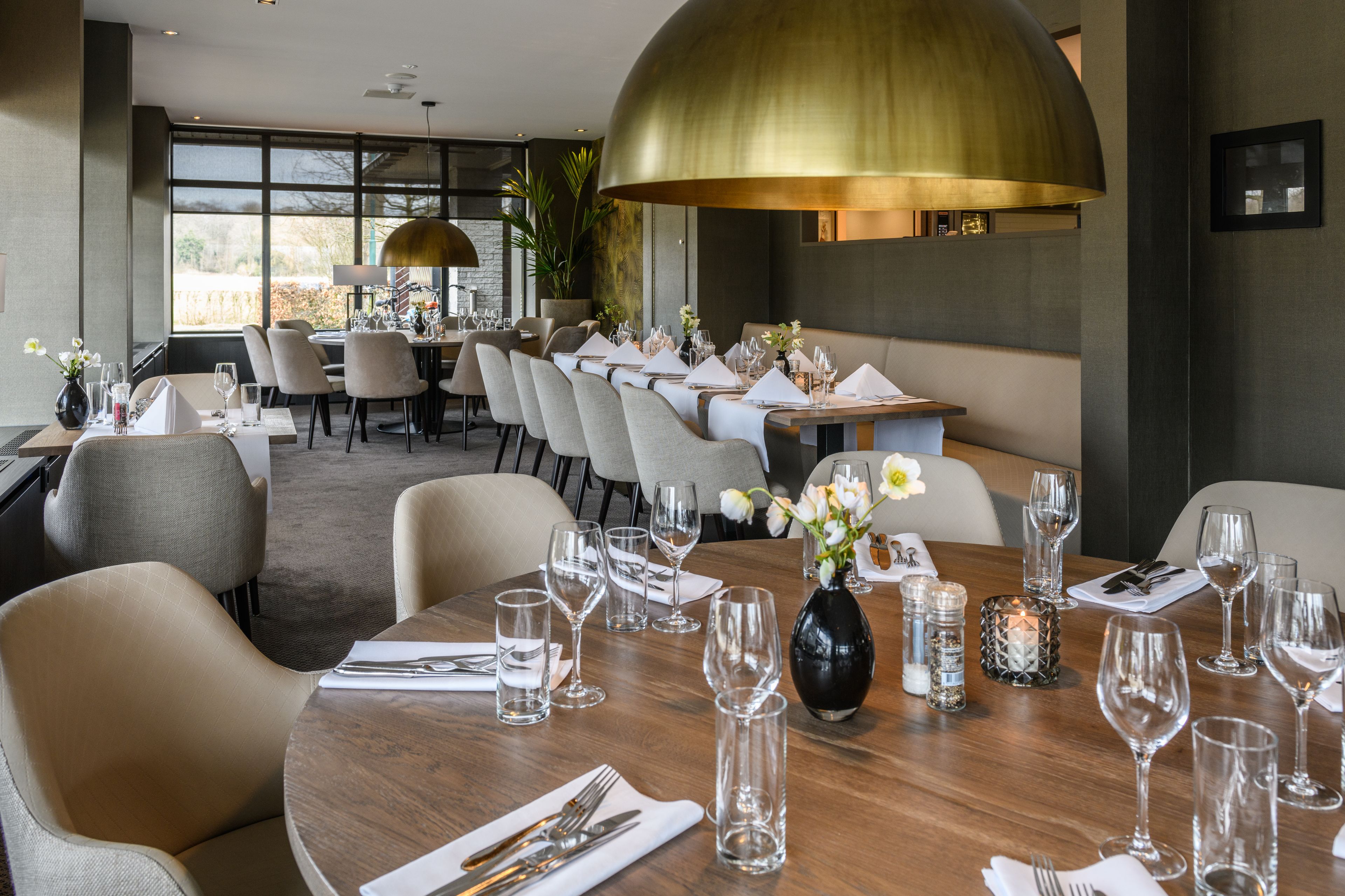 A modern dining area with round tables set for a meal, featuring neutral-toned chairs and a large, dome-shaped light fixture above.