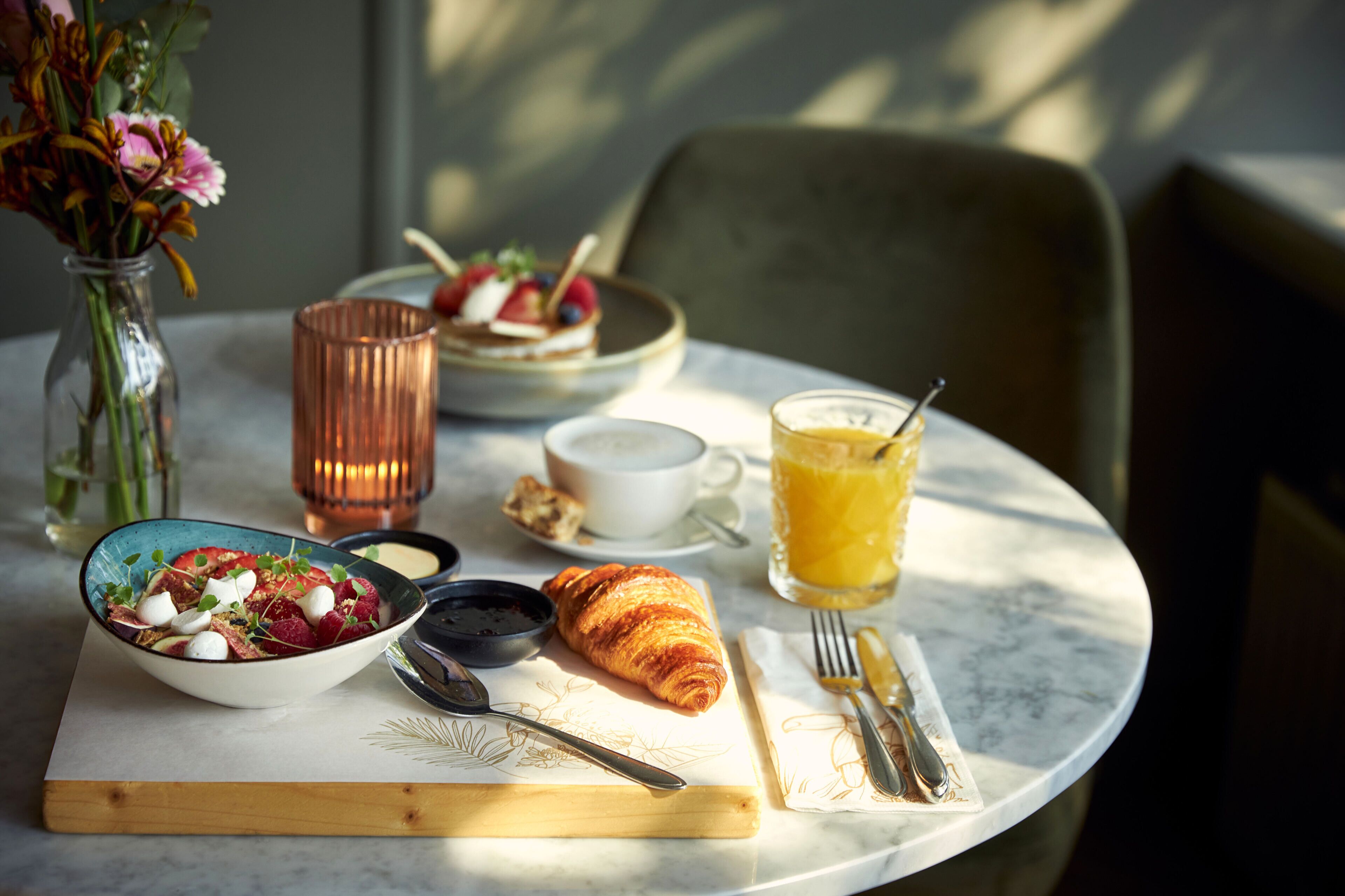 Ein Frühstücksbuffet mit einem Croissant, Obstsalat, Kaffee und Orangensaft auf einer Marmortischplatte.