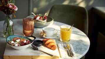 A breakfast setting with a croissant, fruit salad, coffee, and orange juice on a marble table.