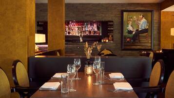 A restaurant with a wooden table set for dining, a bar in the background, and a painting on the wall.