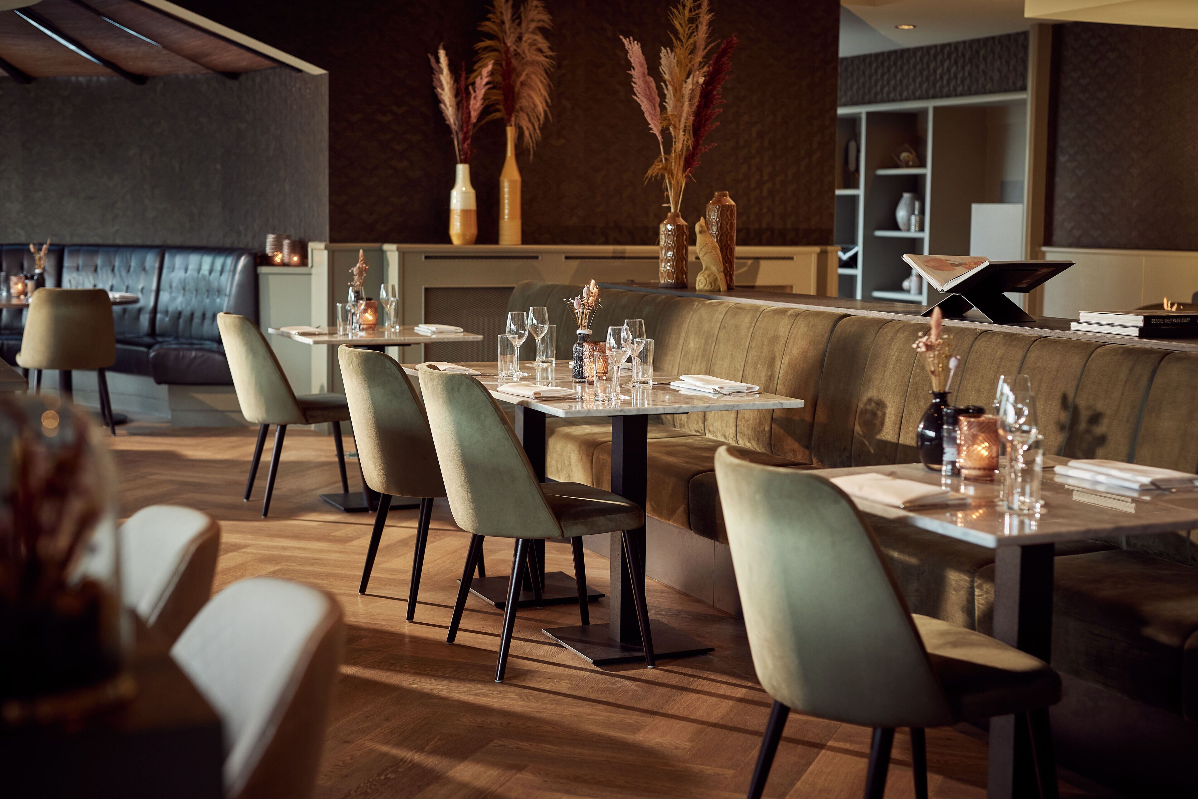 Un intérieur de restaurant moderne avec des banquettes et des tables, un plancher en bois et des plantes décoratives.