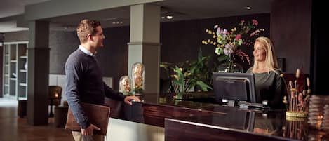 A reception desk with a modern design, a vase of flowers, and a digital screen.