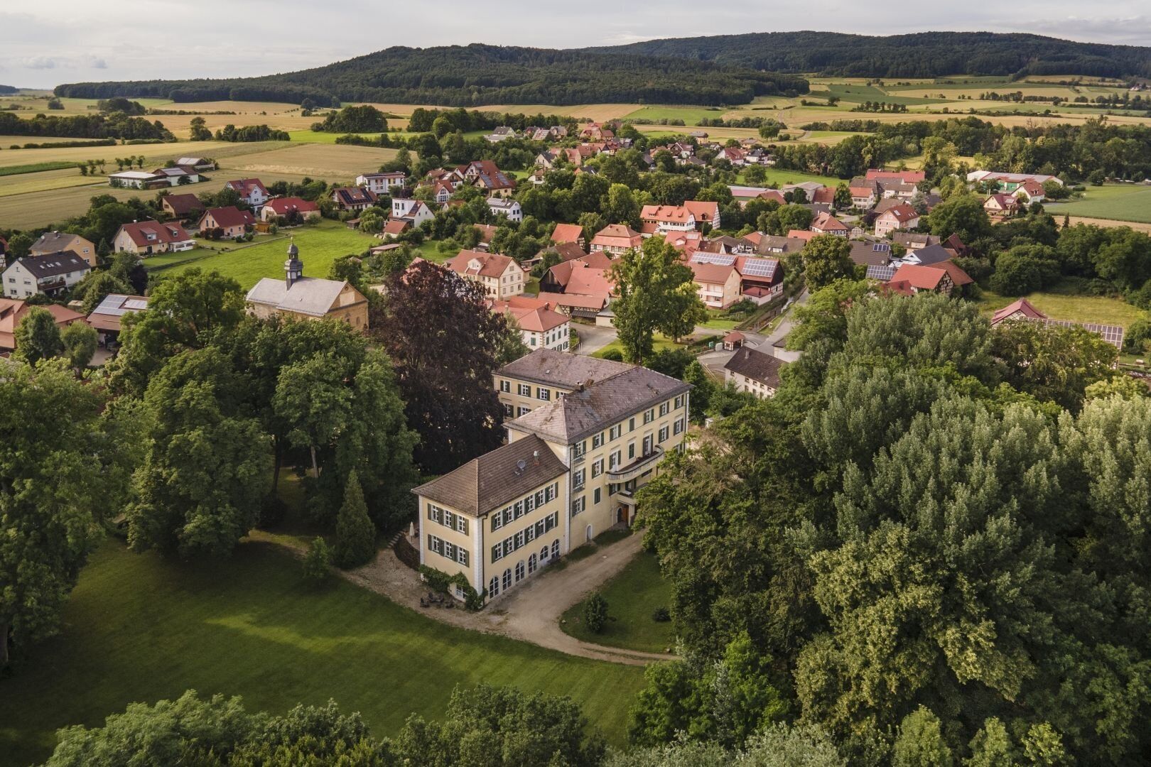 Vue aérienne d’un village rural, avec ses maisons traditionnelles, entouré de verdure et de champs.