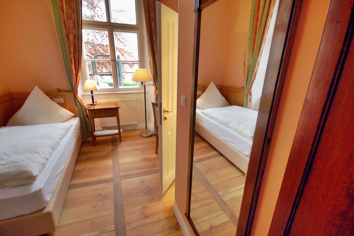 A bedroom with two single beds, a bedside table with a lamp, a radiator, and a window with curtains.