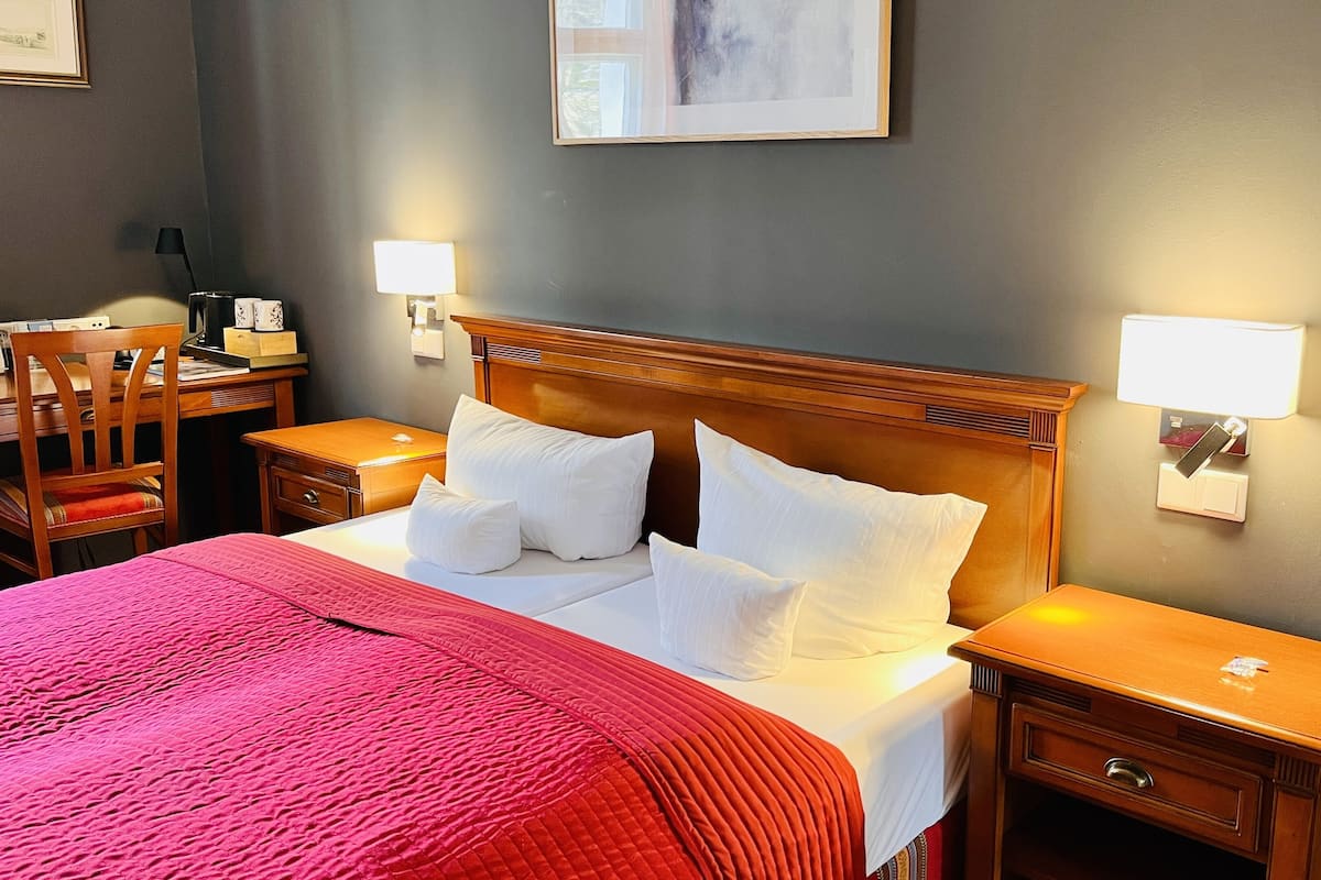 A hotel room with a large bed, two bedside tables, a desk, and a chair.