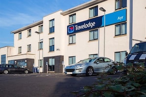 A Travelodge hotel with a modern facade, multiple windows, and a parking area with cars. - Travelodge Ayr (Ayr)