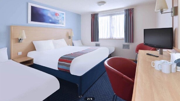 A hotel room with a large bed, two bedside tables, a desk with a chair, a television, and a window with curtains. - Travelodge Ayr (Ayr)