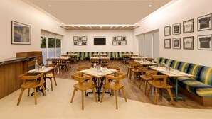 Un grand espace dédié à la salle à manger, avec plusieurs tables et chaises, un comptoir et un canapé aux couleurs vives.