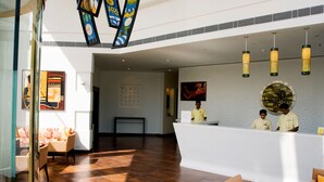 Un espace d’accueil avec un comptoir blanc, deux employés, un grand tableau abstrait et un mur orné de motifs.
