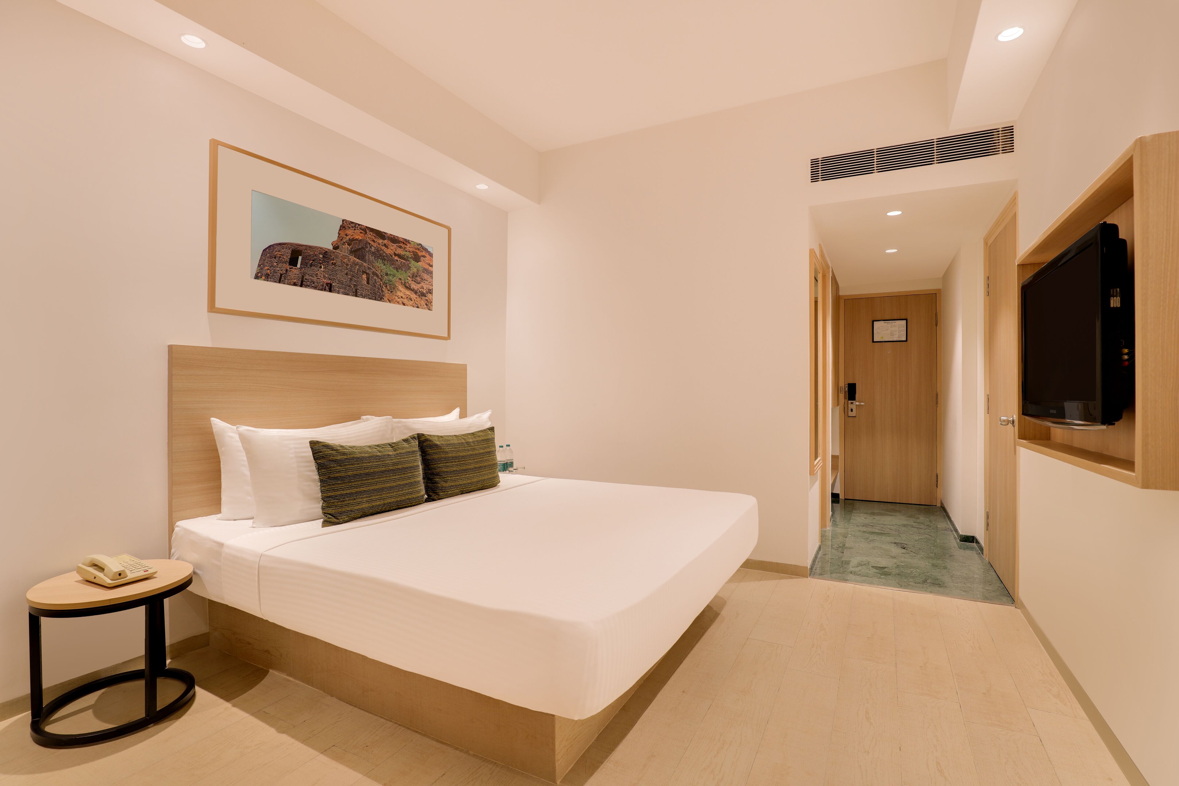 A modern hotel room with a large bed, a bedside table with a phone, a framed picture on the wall, and a TV on the wall.