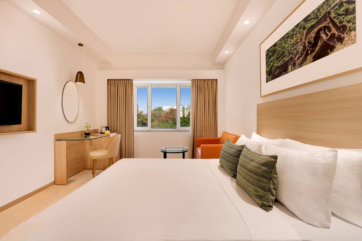 A modern hotel room with a large bed, a desk, a chair, and a television.