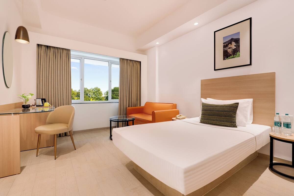 A hotel room with a bed, a desk, a chair, a small table, and a window with curtains.