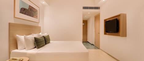 Habitación de hotel moderna con una cama grande, una mesita de noche, un televisor montado y un cuadro enmarcado en la pared.