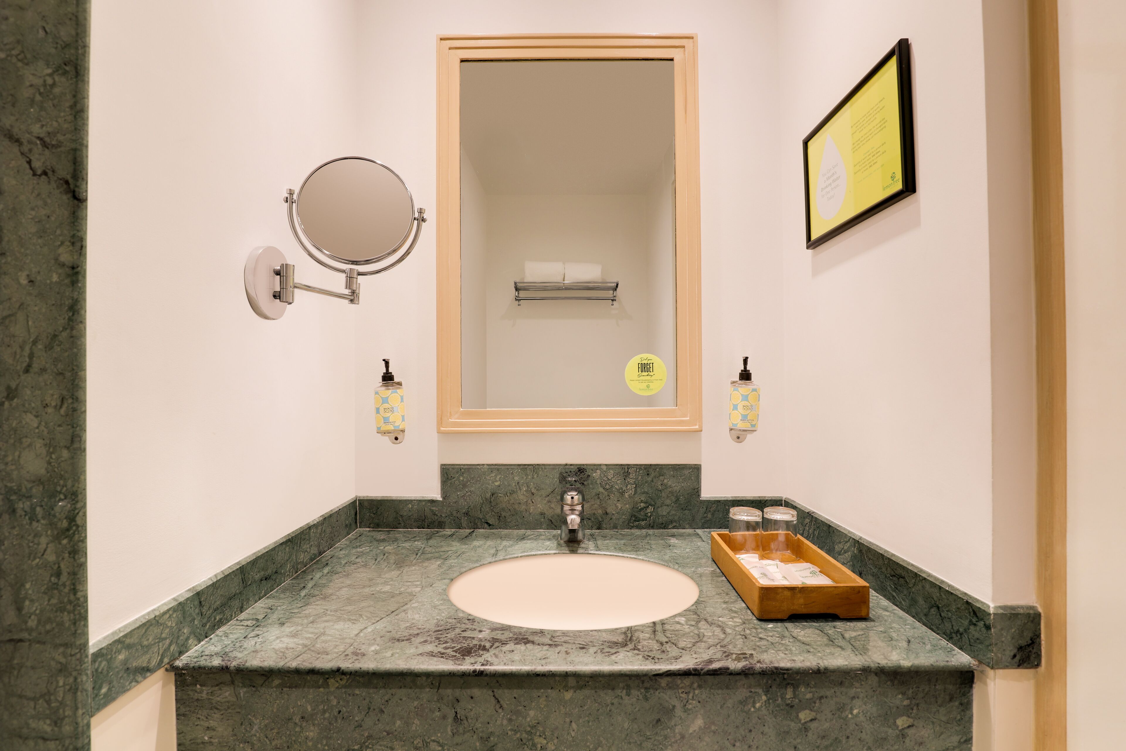 A bathroom with a marble sink, a mirror, a framed informational sign, and two wall-mounted soap dispensers.