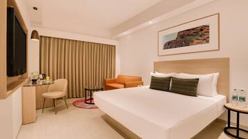 Una habitación de hotel con una cama grande, un escritorio con una silla, una mesita con otra silla y un televisor en la pared izquierda.