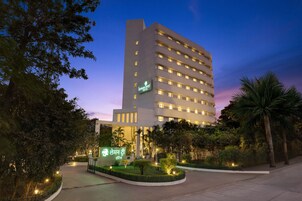 A modern hotel with a prominent sign, surrounded by well-maintained landscaping and palm trees.
