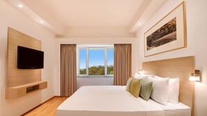 Une chambre d’hôtel moderne avec un grand lit, un téléviseur fixé au mur, un téléphone sur la table de chevet et une fenêtre avec des rideaux.