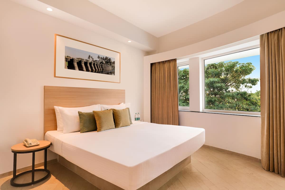 A hotel room with a large bed, a bedside table with a phone, a framed picture on the wall, and a window with curtains.