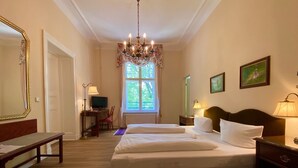 A hotel room with a large bed, a desk with a chair, a television, and a chandelier. - Hotel - Restaurant Kronprinz (Falkensee)
