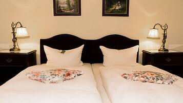 Una cama doble con cubrecamas florales, dos mesitas de noche con lámparas, y dos cuadros en la pared.