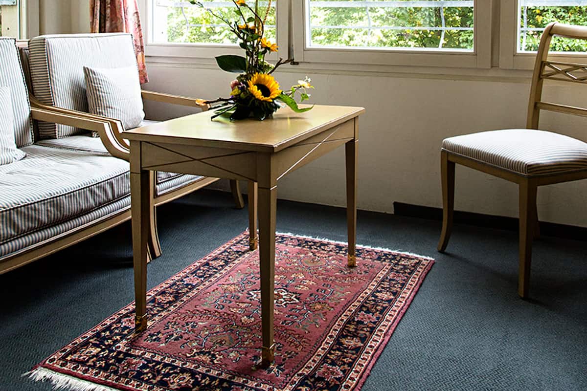 A room with a wooden table, a floral-patterned rug, a sofa, and two chairs.