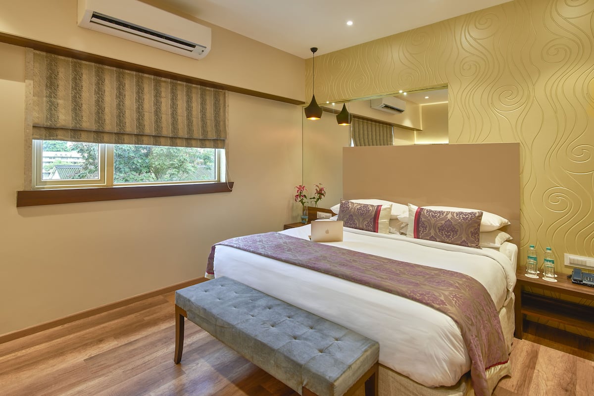 A modern bedroom with a large bed, a bench, an air conditioner, a window with curtains, and a decorative wall.