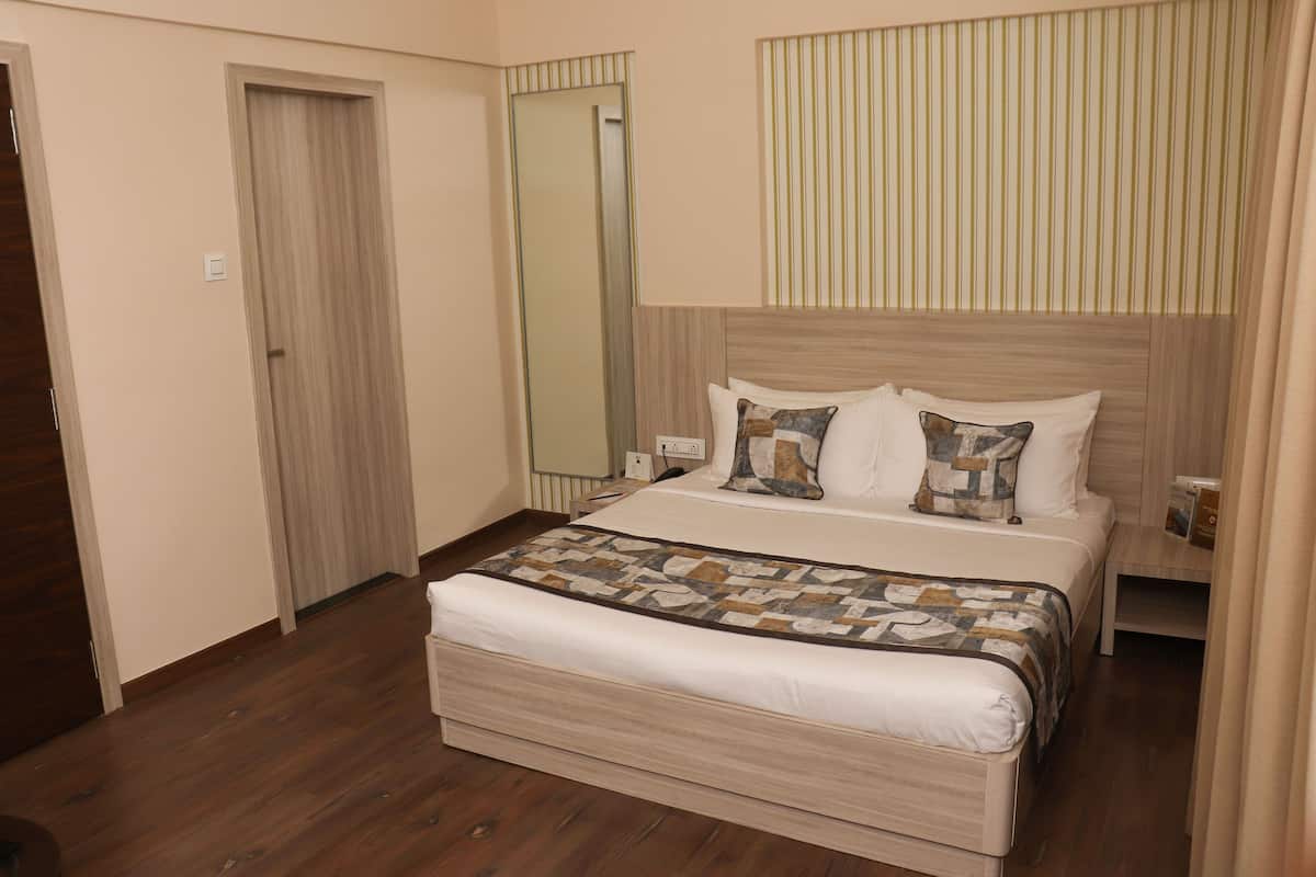A neatly arranged bedroom with a wooden floor, a bed with a patterned bedspread, a bedside table, and a mirror on the wall.