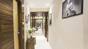 A hotel hallway with wooden doors, a bench with a vase of flowers, and framed pictures on the walls. - Bawa Regency (Mumbai)