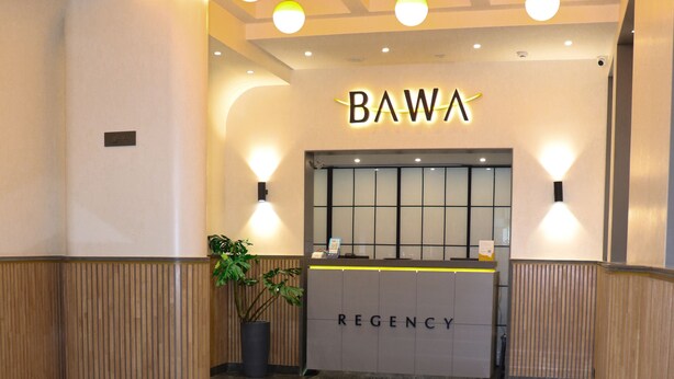 A reception area with a 'BAWA' sign, a reception desk labeled 'REGENCY', and a seating area with a blue chair and a small table. - Bawa Regency (Mumbai)