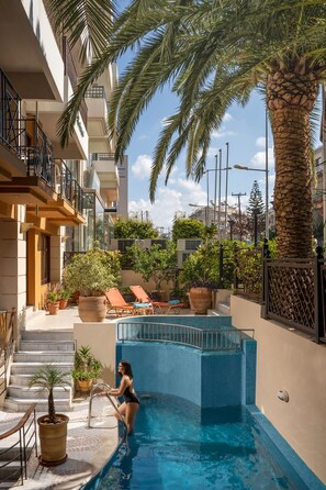 A swimming pool with a palm tree, lounge chairs, and potted plants. - Brascos (Rethymno)