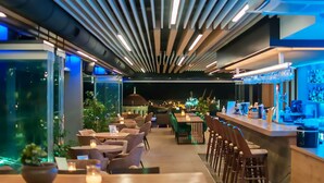 Un restaurante moderno con barra, mesas y sillas de madera, y vistas panorámicas de la ciudad.