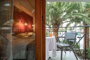A room with a bed, a table with a drink, and a balcony with chairs and a palm tree. - Brascos (Rethymno)