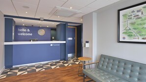 A reception area with a blue wall, a clock, a reception desk, and a map on the wall. - Travelodge Caterham Whyteleafe (Whyteleafe)