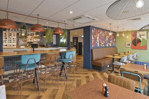 A modern restaurant interior with a bar area, seating arrangements, and decorative wall art. - Travelodge Caterham Whyteleafe (Whyteleafe)