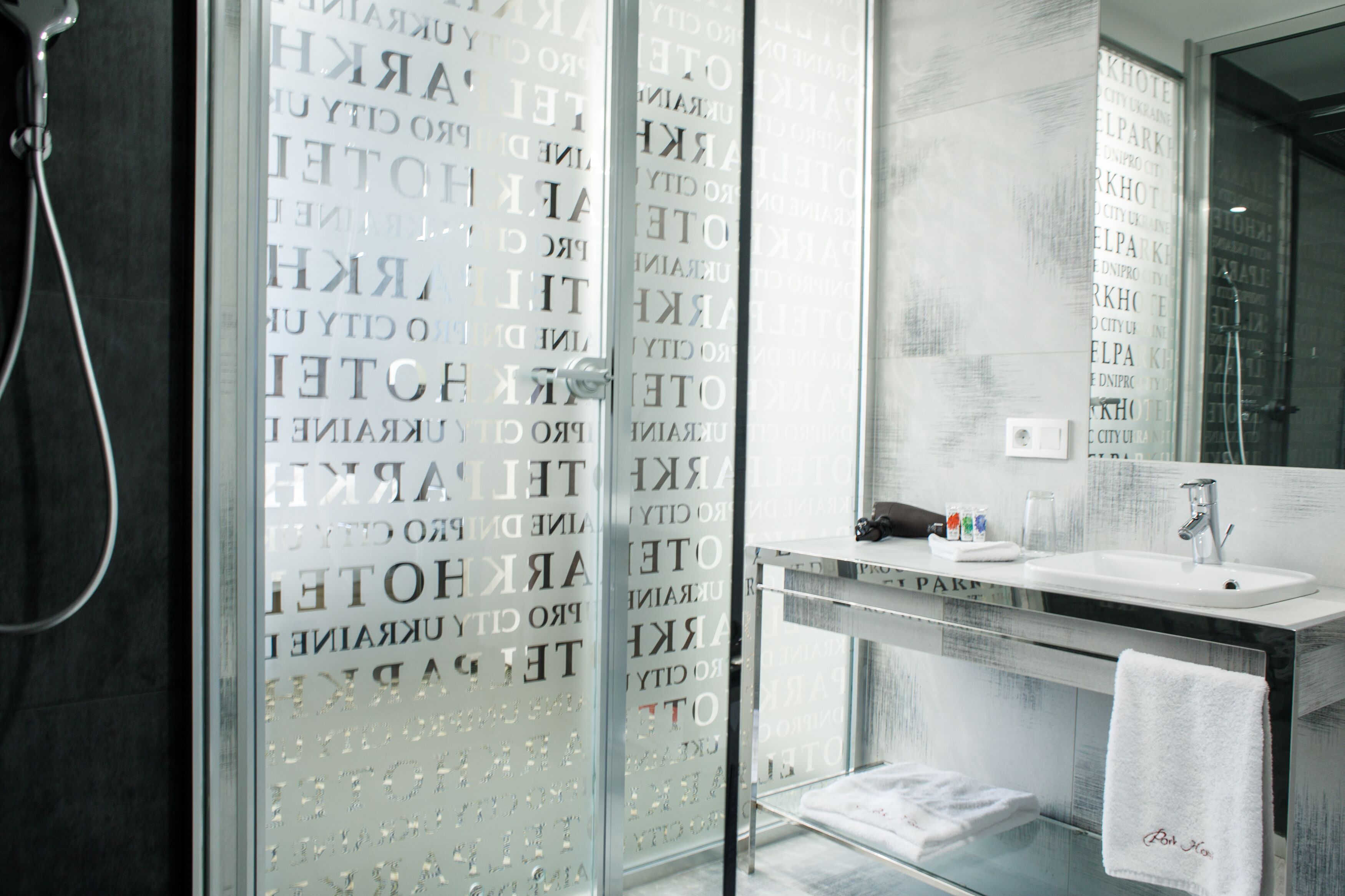 A modern bathroom with a glass shower enclosure, a white sink, and a towel rack.