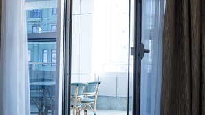 A room with a blue patterned carpet, a sliding glass door leading to an outdoor area with a table and chairs, and a view of buildings in the background. - Park Hotel (Dnipro)