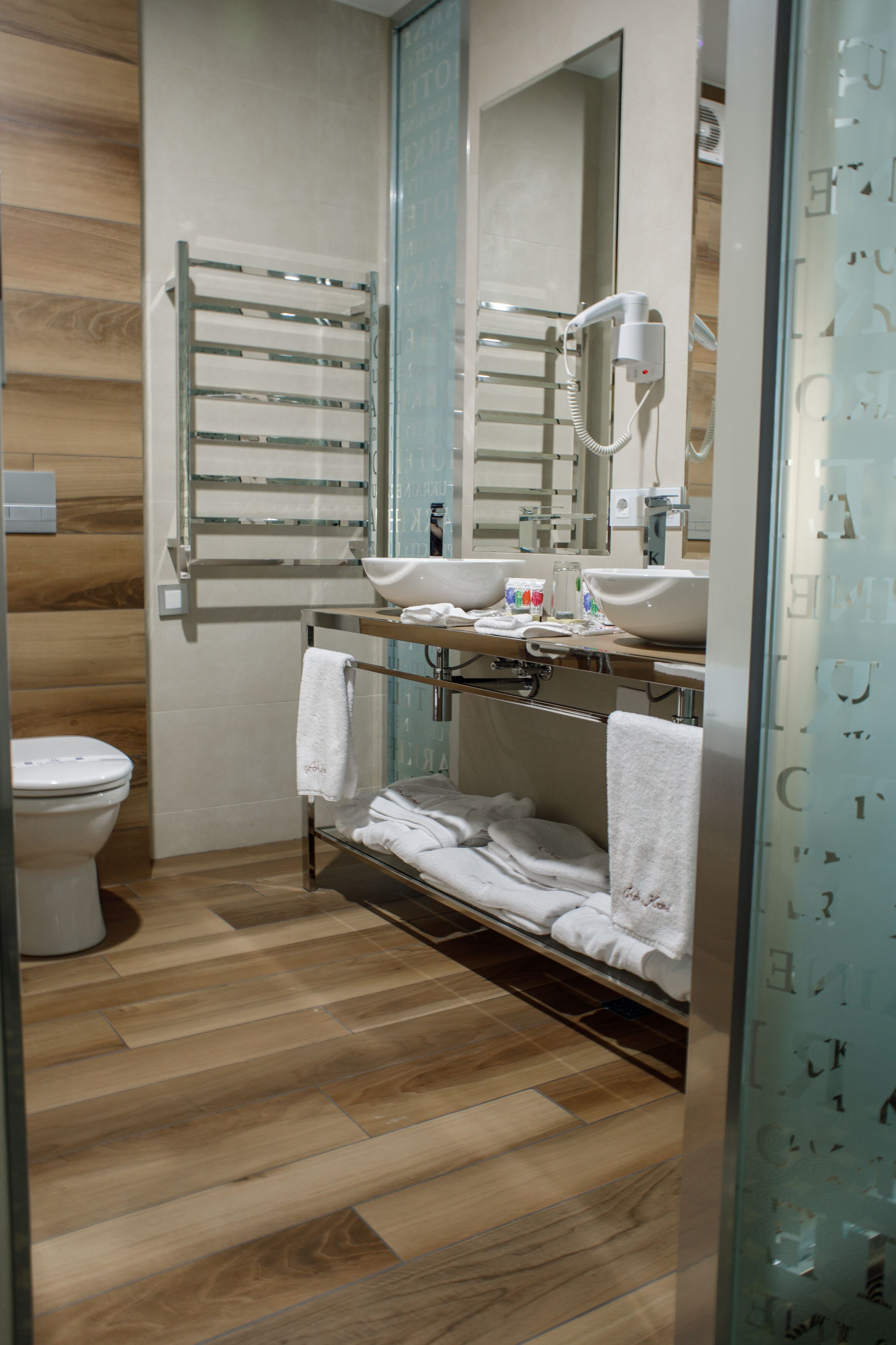 A modern bathroom with a wooden floor, a glass shower enclosure, a white sink, and a towel rack.