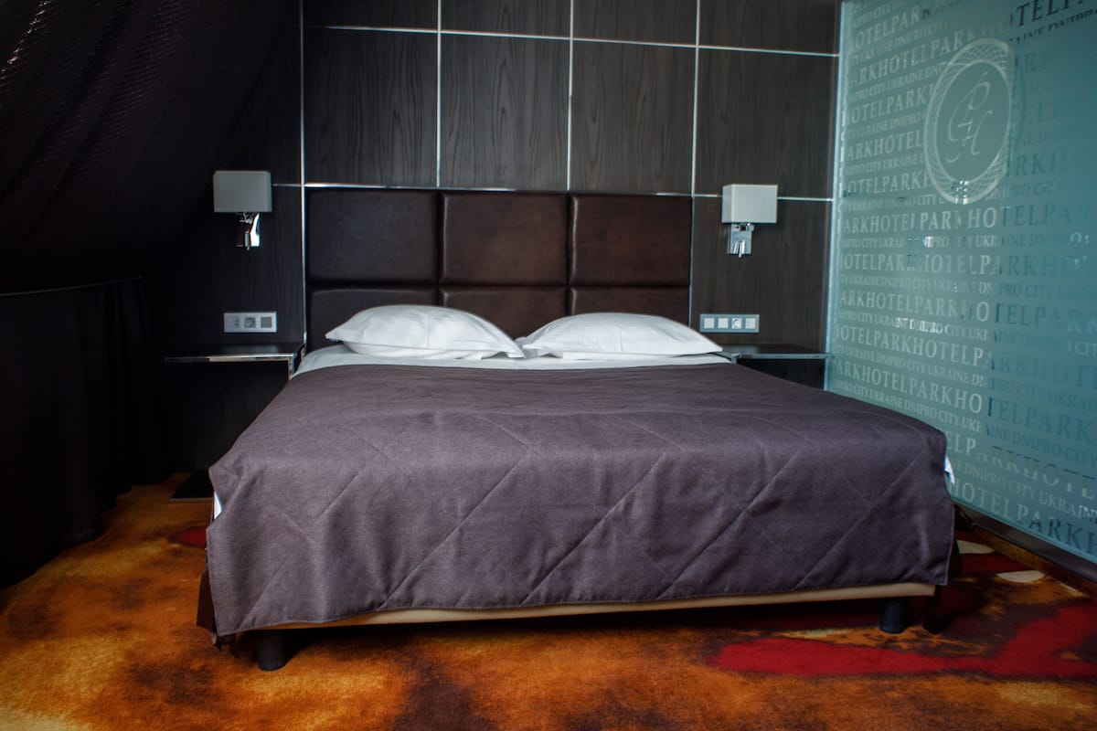 Ein Hotelzimmer mit einem großen Bett, einem Kopfteil mit Gittermuster, zwei Nachttischlampen und einer Wand mit sich wiederholendem Text.