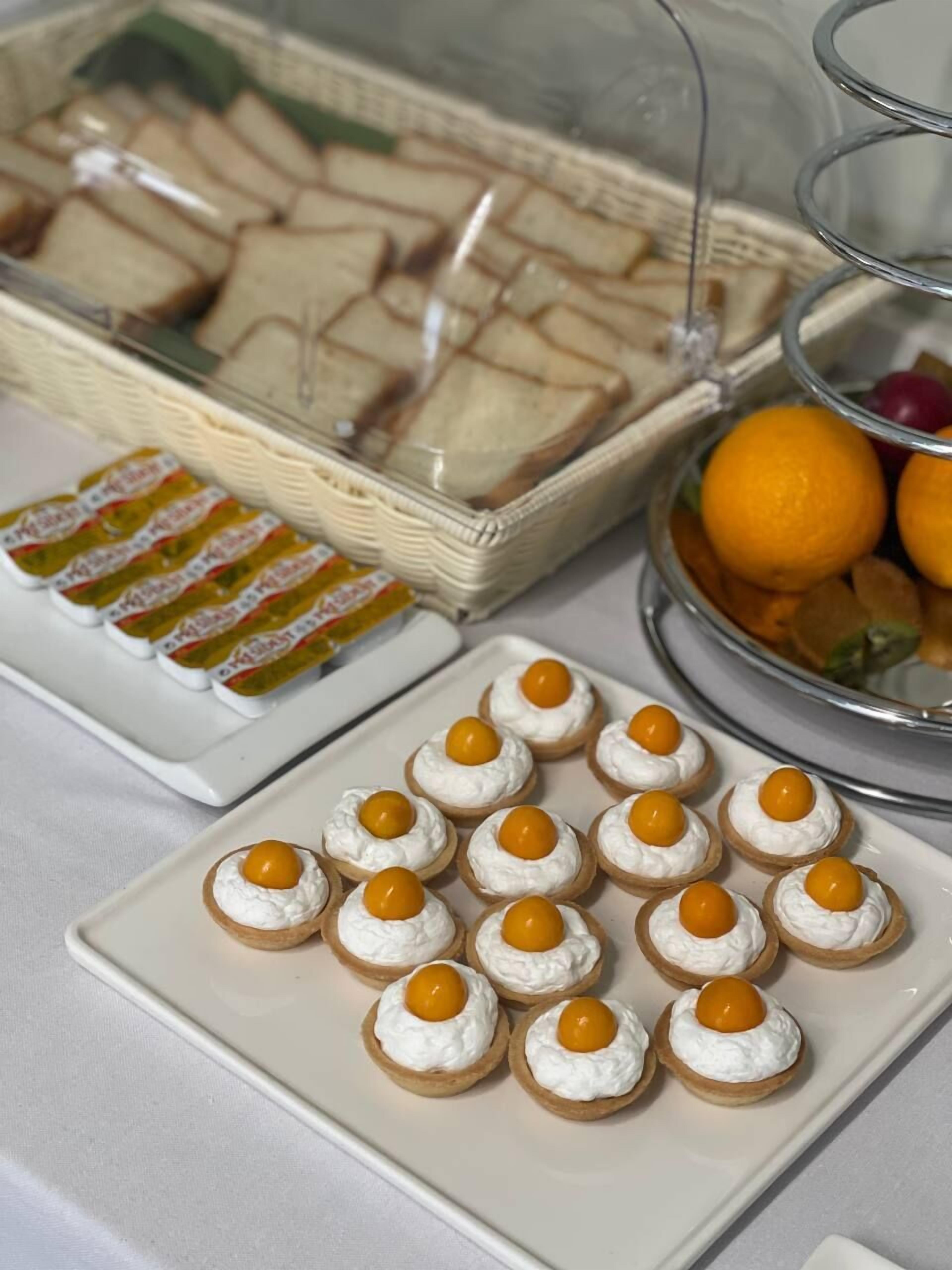 A buffet table with various food items including sandwiches, mini quiches, and a fruit bowl.