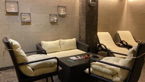 A spa room with a massage table, two wicker chairs, a small table with magazines, and wall-mounted shelves with decorative items. - Park Hotel (Dnipro)