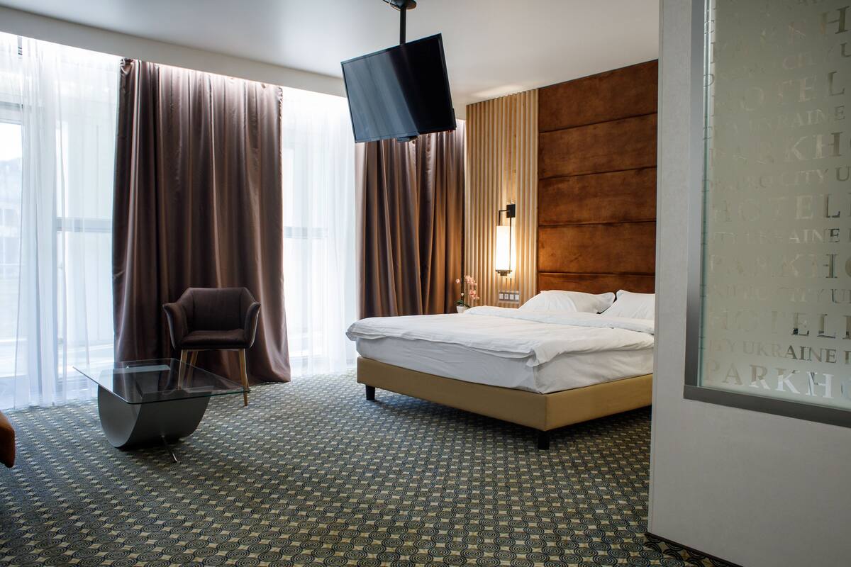 Ein Hotelzimmer mit einem Bett, einem Fernseher, einem Sessel und einem gemusterten Teppich.